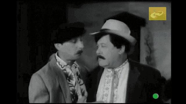 two men are talking in a black and white photo with a green circle in the corner that says c2