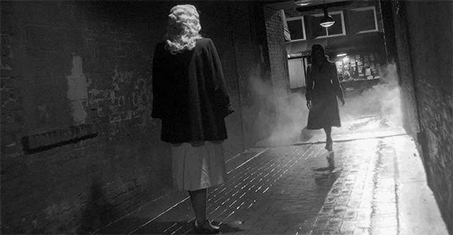 two women are walking down a dark hallway with smoke coming out of it .