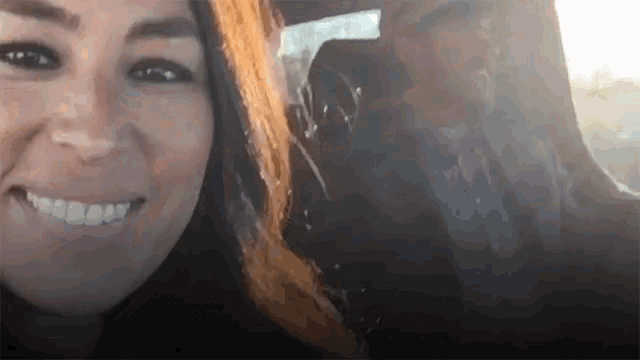 a woman smiles while sitting in a car with a man behind her