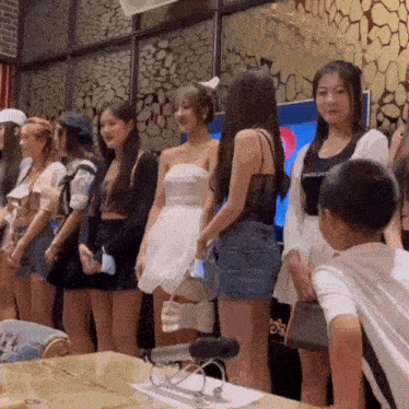 a group of young women are standing around a table with a boy standing in front of them .