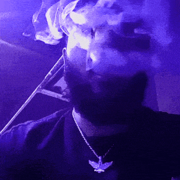 a man wearing a necklace with an angel pendant is smoking a cigarette in a dark room .