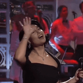 a woman in a black dress is singing into a microphone with her hands in the air