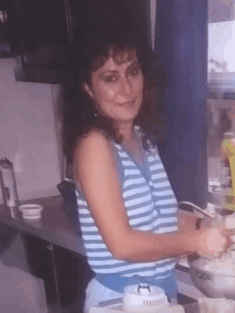 a woman in a blue and white striped tank top is cooking in a kitchen