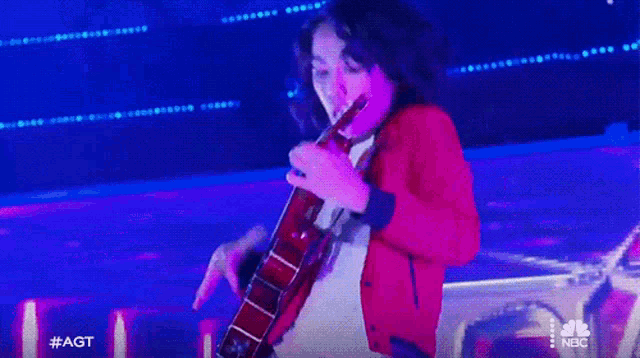 a man in a red jacket is playing a guitar in front of a blue background .