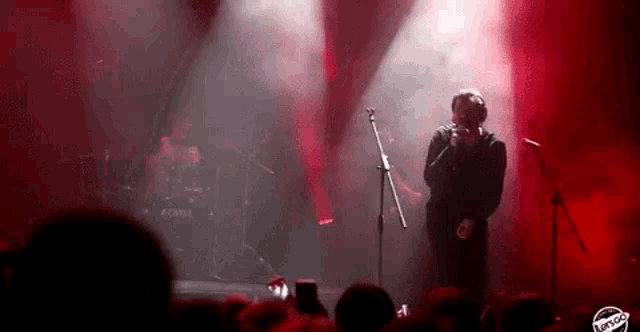 a man is singing into a microphone on a stage in front of a crowd of people .