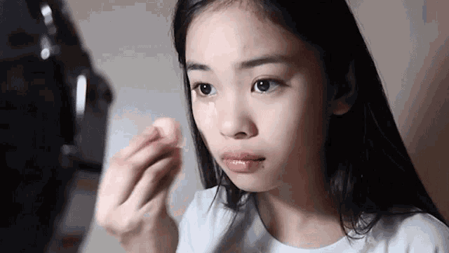 a young girl is looking at herself in a mirror while applying makeup .