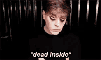 a man with black eyes and a black shirt is standing in a dark room and says `` dead inside '' .