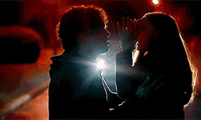 a man and a woman are kissing in the dark with a car headlight shining on them .