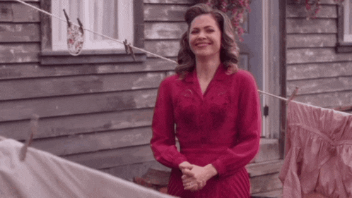 a woman in a red dress is standing in front of a wooden building .