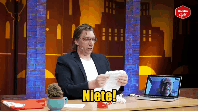 a man sits at a table with a laptop and a sign that says niete