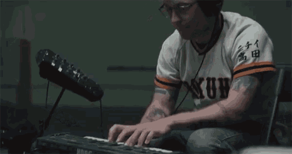 a man wearing a shirt that says nun on it is playing a keyboard
