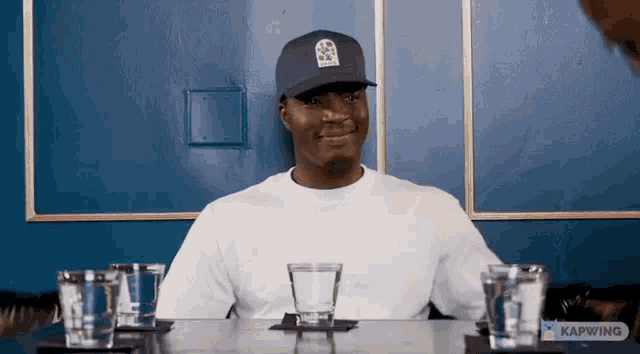 a man wearing a blue hat is sitting at a table with two glasses of water