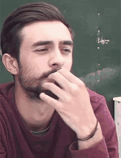 a man with a beard is covering his mouth with his hand while wearing a maroon shirt .