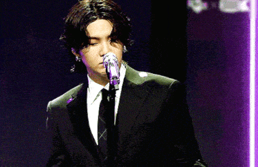 a man in a suit is singing into a microphone on a stage