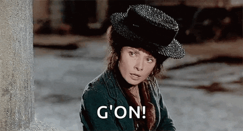 a woman wearing a hat and a jacket is sitting next to a wall and saying g ' on .