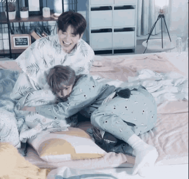 two boys are laying on a bed and one of them is wearing a pajama with palm leaves on it