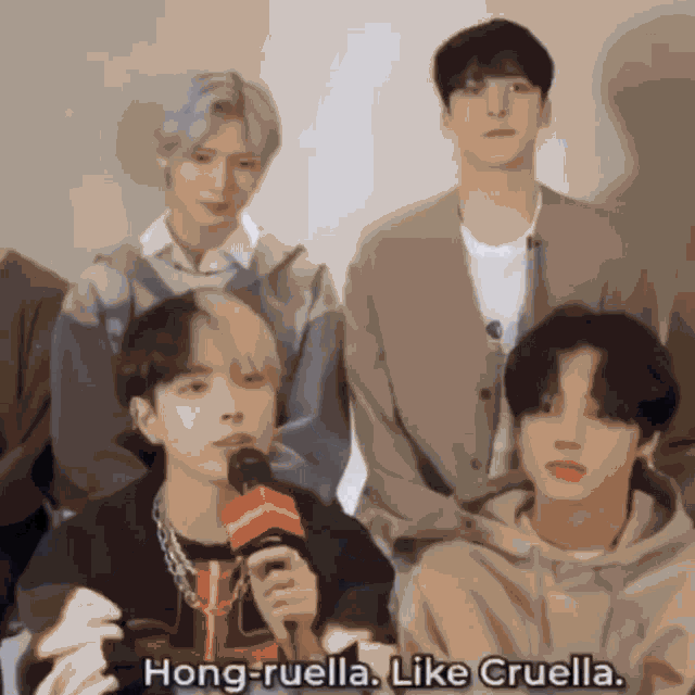 a group of young men are sitting around a man holding a microphone and saying hong-ruella like cruella .