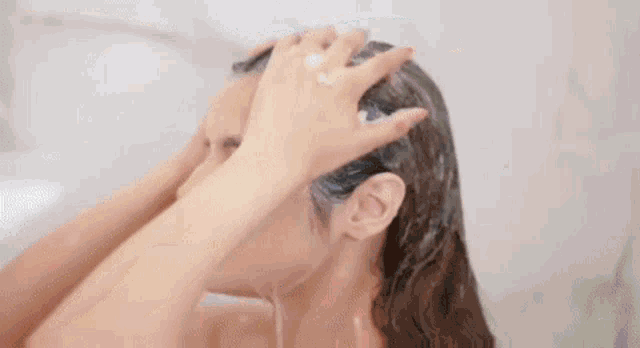 a woman is washing her hair in a shower with shampoo .