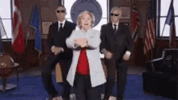 a woman is dancing with two men in suits in a room .