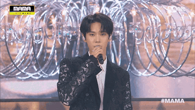 a man in a suit is singing into a microphone while standing in front of a wall of barbed wire ..
