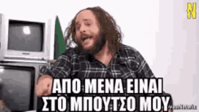 a man with long hair and a beard is sitting in front of two televisions and making a funny face .