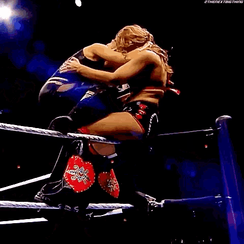 two women are wrestling in a ring and one of them is laying on the floor .