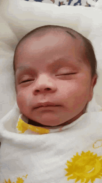 a baby wrapped in a white blanket with yellow flowers on it
