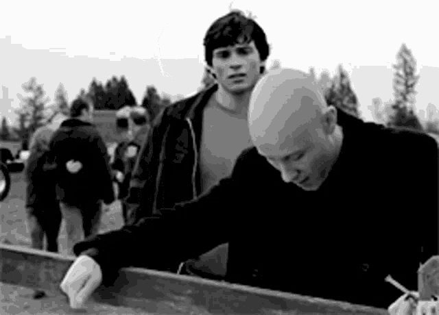 two bald men are standing next to each other in a field .