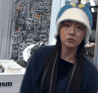 a woman wearing a cat hat is standing in front of a wall that says ism