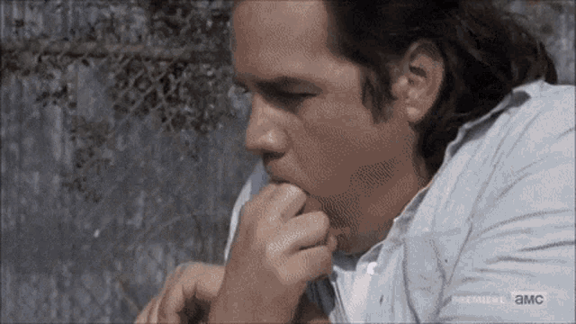 a man in a blue shirt is biting his nails in front of a chain link fence .