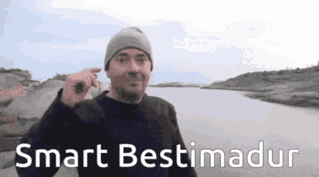 a man wearing a beanie is pointing at something in front of a river and the words smart bestimadur