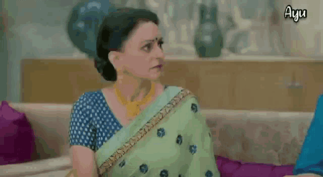 a woman in a green saree is sitting on a couch and says bhat