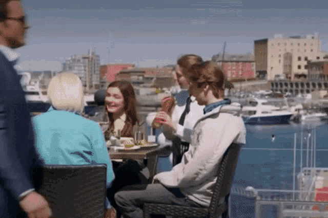 a group of people are sitting at a table in a harbor