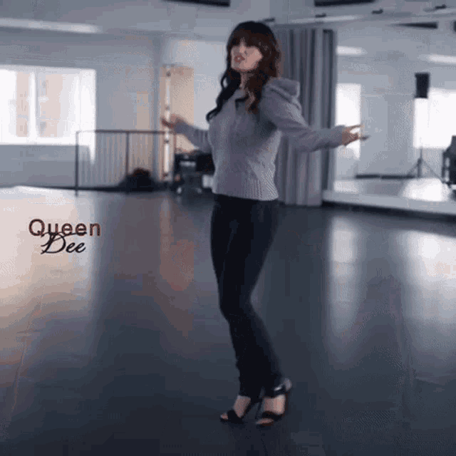 a woman in a purple sweater is dancing in a dance studio with queen dee written on the bottom