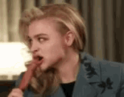 a woman in a blue jacket is eating a red candy bar .