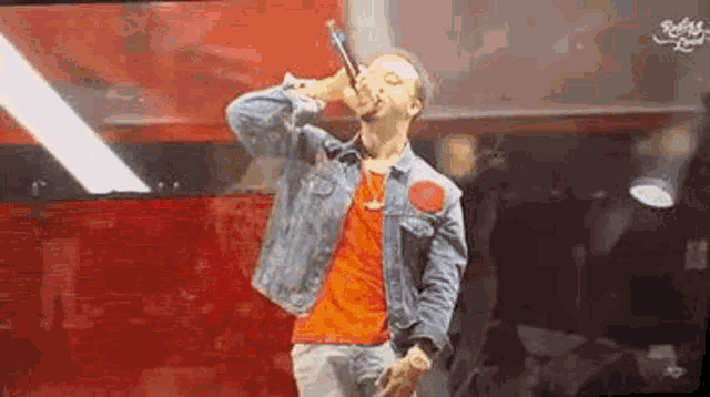 a man in a denim jacket is singing into a microphone while standing on a stage .