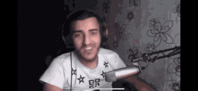 a man wearing headphones and a white shirt is sitting in front of a microphone and smiling .