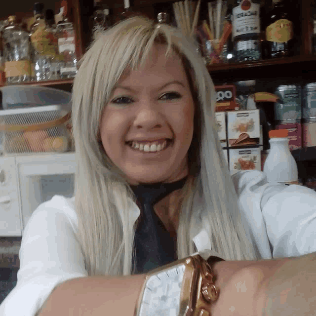 a woman wearing a watch is smiling in front of a shelf full of bottles including one that says ' cream '