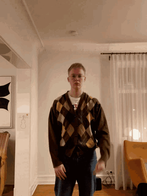 a man wearing a plaid sweater and a white shirt with the letter t on it
