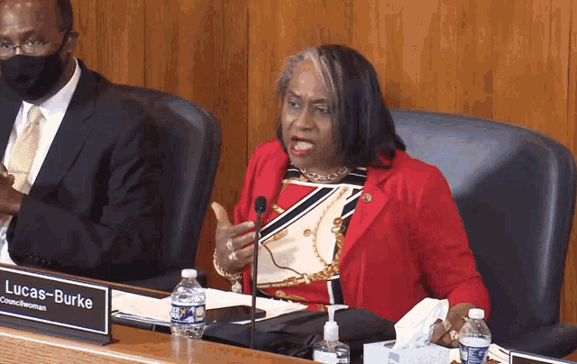 a woman in a red jacket sits at a table with a name plate that says burke