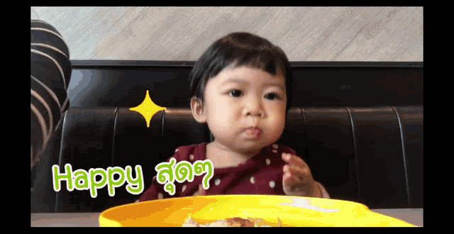 a little girl is sitting at a table with a plate of food and the words happy written on it