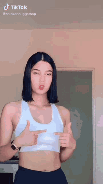 a woman in a white crop top is pointing at herself .
