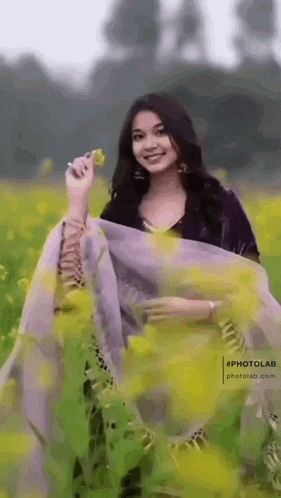 a woman is standing in a field of yellow flowers and holding a flower .