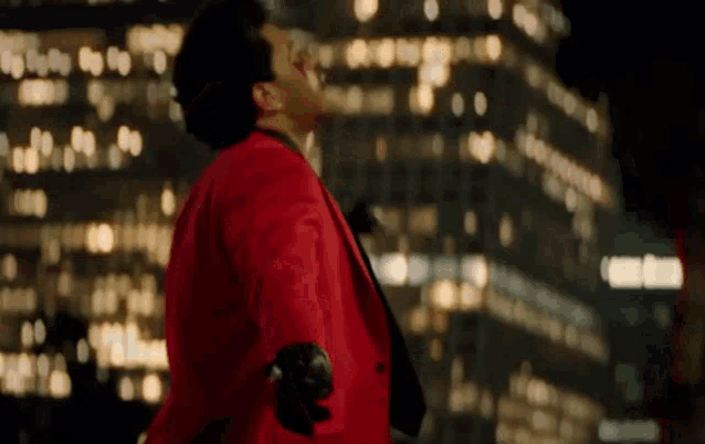 a man in a red suit and tie is dancing in front of a city at night .