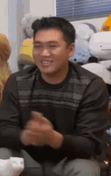 a man in a black sweater is sitting in front of stuffed animals and smiling