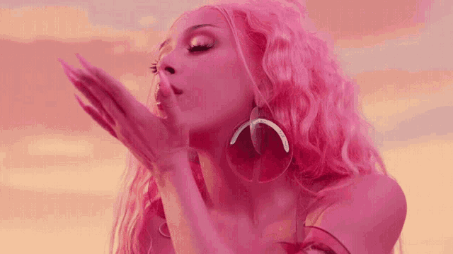 a woman with pink hair and earrings blowing a kiss