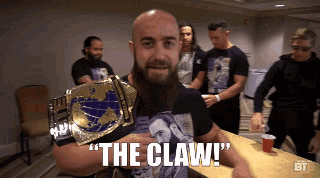 a bald man with a beard is holding a world heavyweight wrestling championship belt and says " the claw "