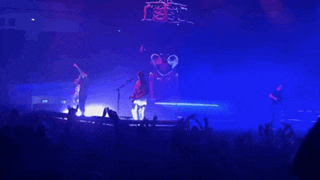 a group of people are dancing on a stage in front of a crowd with a blue light behind them