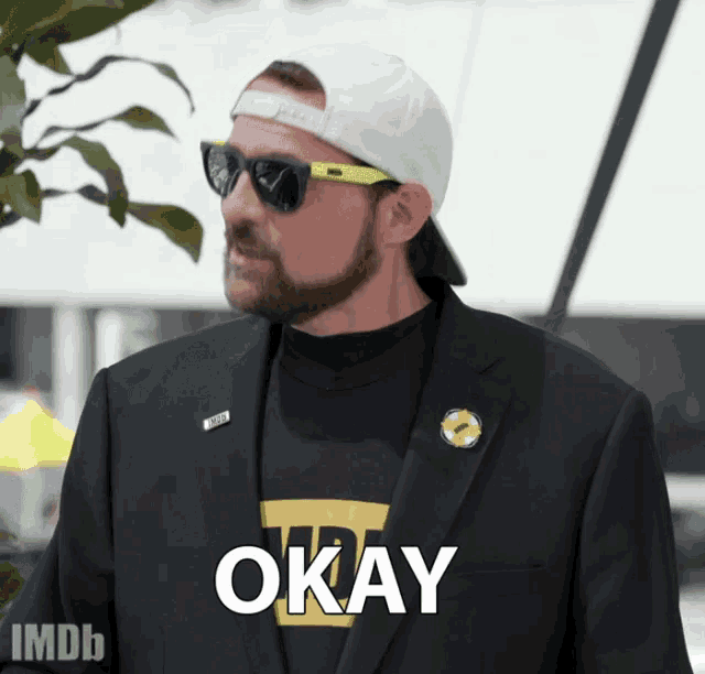 a man wearing sunglasses and a hat with the word okay on his shirt