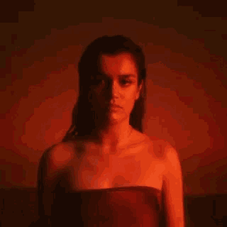 a woman in a strapless top is standing in a dark room with a red light behind her .